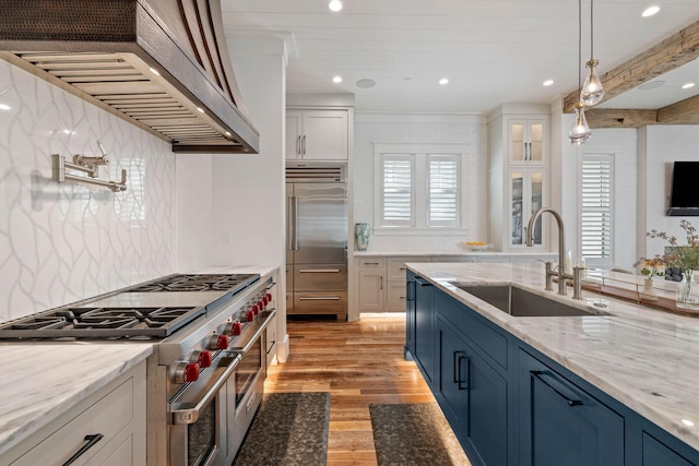 kitchen featuring white cabinets, high end appliances, wall chimney exhaust hood, and sink