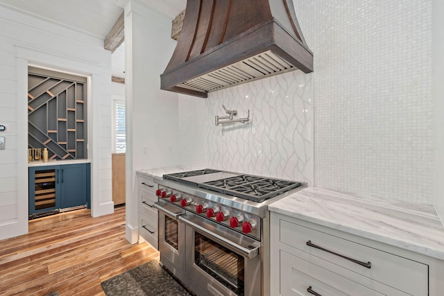 kitchen featuring beverage cooler, light stone counters, range with two ovens, custom exhaust hood, and light wood-type flooring