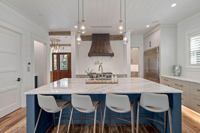 kitchen with custom exhaust hood, a spacious island, hardwood / wood-style flooring, decorative light fixtures, and stainless steel built in refrigerator