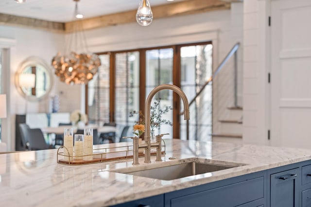 kitchen featuring blue cabinetry, light stone countertops, sink, and hanging light fixtures