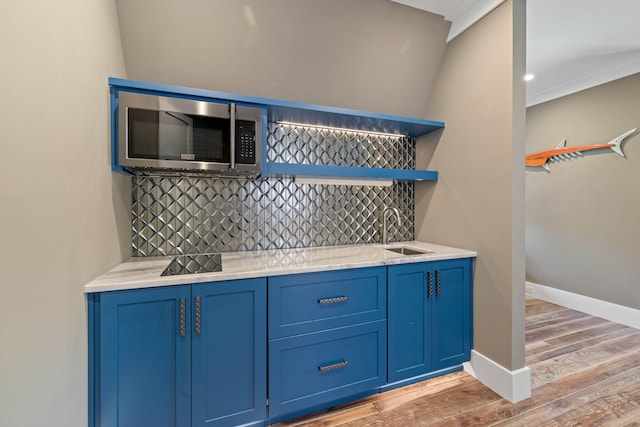 bar with blue cabinetry, sink, tasteful backsplash, and light wood-type flooring