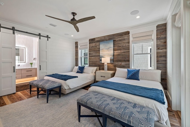 bedroom with ceiling fan, a barn door, crown molding, wood walls, and hardwood / wood-style flooring