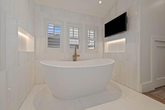 bathroom with lofted ceiling, a tub to relax in, and tile walls