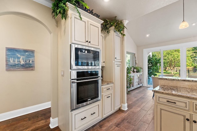 kitchen featuring dark wood-type flooring, vaulted ceiling, light stone countertops, appliances with stainless steel finishes, and cream cabinetry