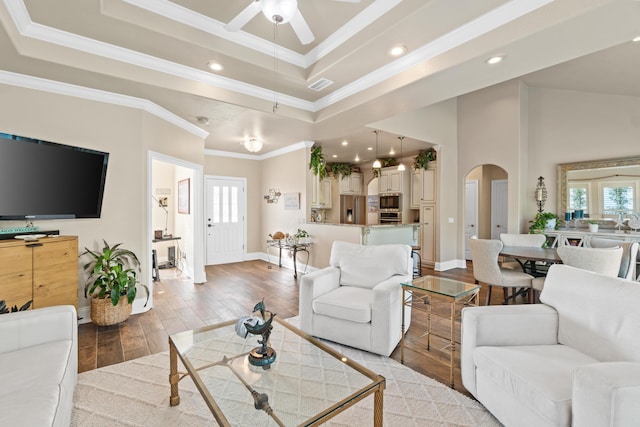 living room with light wood-type flooring, a raised ceiling, ceiling fan, and ornamental molding