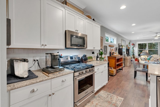 kitchen featuring appliances with stainless steel finishes, tasteful backsplash, ornamental molding, white cabinets, and light hardwood / wood-style floors