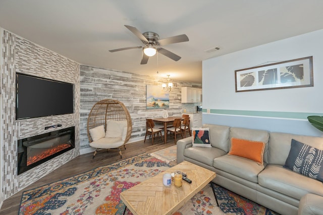 living room featuring a stone fireplace, wood-type flooring, and ceiling fan with notable chandelier