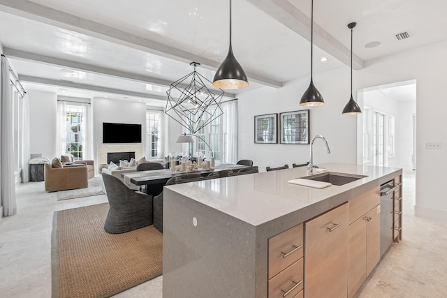 kitchen featuring beam ceiling, sink, an island with sink, and hanging light fixtures