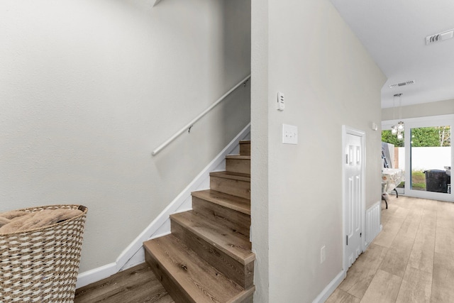 staircase with hardwood / wood-style floors and an inviting chandelier