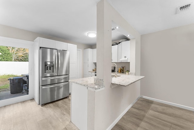 kitchen with light stone counters, light hardwood / wood-style flooring, stainless steel refrigerator with ice dispenser, kitchen peninsula, and white cabinets