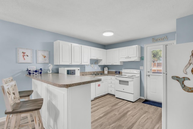 kitchen featuring kitchen peninsula, white appliances, light hardwood / wood-style flooring, white cabinetry, and a breakfast bar area