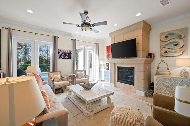 living room featuring french doors, ceiling fan, crown molding, a tile fireplace, and light hardwood / wood-style floors