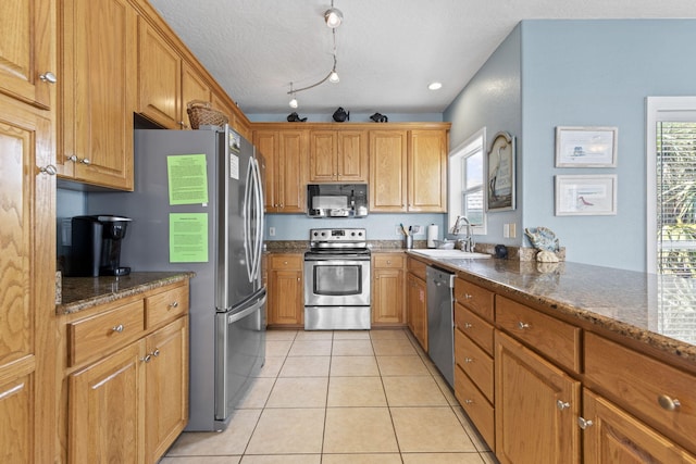 kitchen featuring dark stone counters, sink, light tile patterned floors, a textured ceiling, and stainless steel appliances