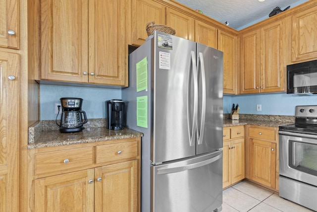 kitchen featuring a textured ceiling, light tile patterned flooring, dark stone countertops, and stainless steel appliances