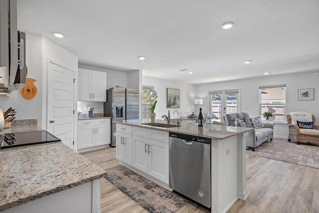 kitchen featuring stainless steel appliances, sink, white cabinets, light hardwood / wood-style floors, and an island with sink