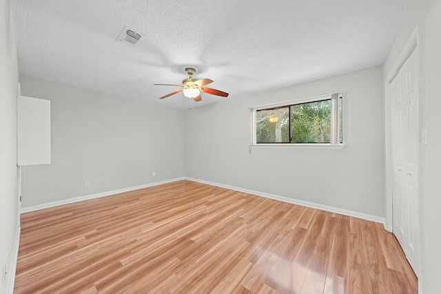 empty room with a textured ceiling, light wood-type flooring, and ceiling fan