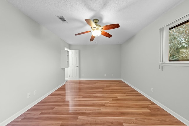 empty room with ceiling fan, light wood-type flooring, and a textured ceiling