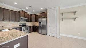 kitchen featuring backsplash, crown molding, dark brown cabinetry, appliances with stainless steel finishes, and a sink