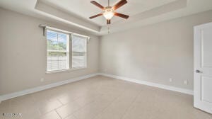 spare room featuring baseboards, a raised ceiling, light tile patterned flooring, and a ceiling fan