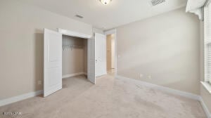 unfurnished bedroom with a closet, baseboards, light carpet, and visible vents