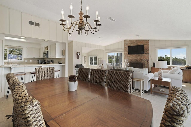 dining space with sink, an inviting chandelier, a textured ceiling, lofted ceiling, and a fireplace