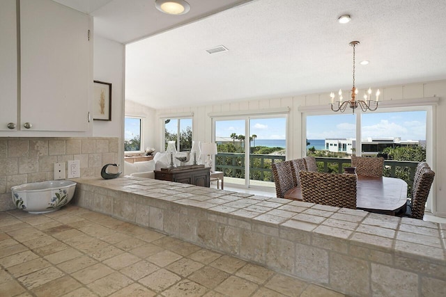 kitchen with tasteful backsplash, a water view, an inviting chandelier, white cabinetry, and hanging light fixtures