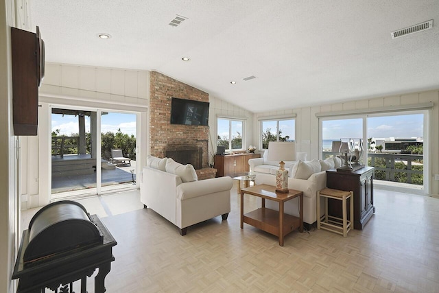 living room featuring a healthy amount of sunlight, lofted ceiling, a textured ceiling, and a brick fireplace