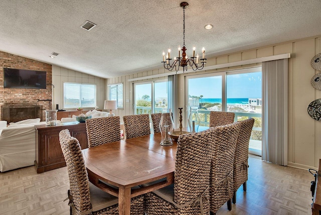 dining room with lofted ceiling, an inviting chandelier, light parquet floors, a water view, and a textured ceiling