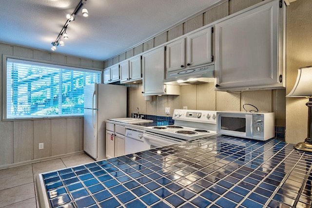 kitchen with white appliances, white cabinets, light tile patterned floors, a textured ceiling, and tile counters