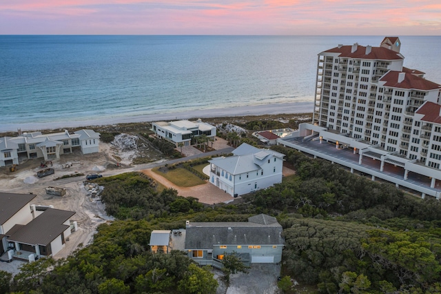 aerial view at dusk featuring a water view and a view of the beach