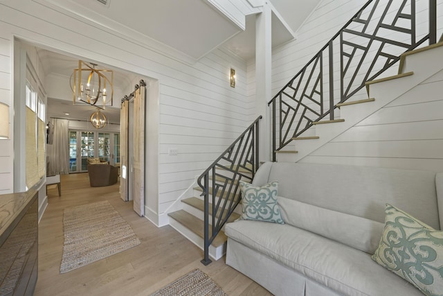 stairway featuring ornamental molding, wood walls, an inviting chandelier, and wood finished floors