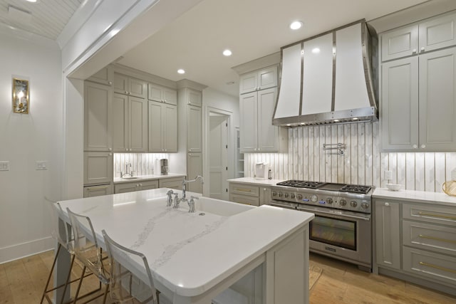 kitchen with sink, stainless steel range, wall chimney range hood, a kitchen breakfast bar, and a center island with sink