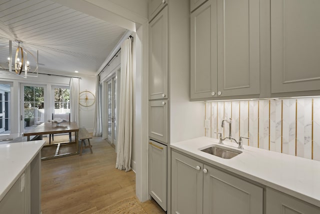 kitchen with light stone countertops, sink, an inviting chandelier, decorative light fixtures, and light wood-type flooring