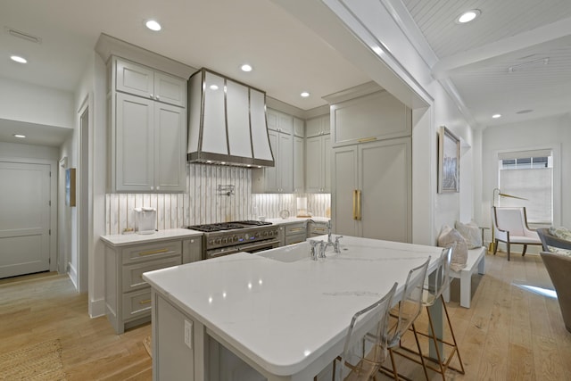 kitchen featuring light wood-type flooring, high end stove, a large island, and wall chimney range hood