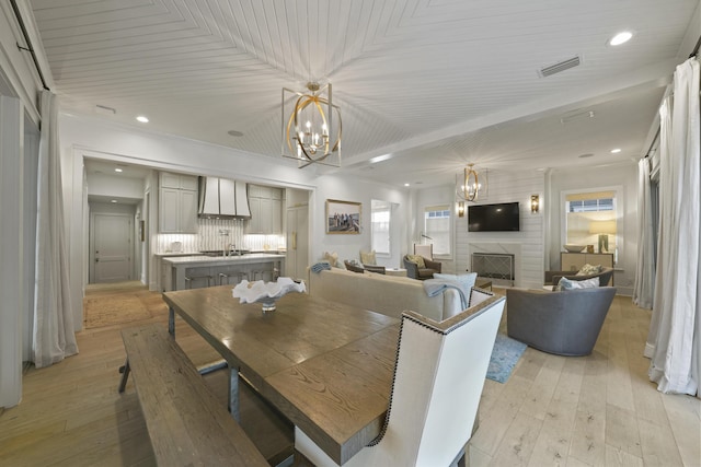 dining space featuring an inviting chandelier, ornamental molding, light wood-type flooring, a fireplace, and wood ceiling