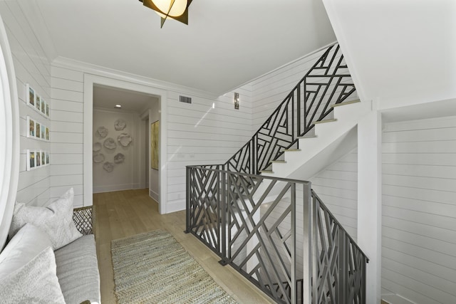 stairway featuring wood-type flooring, ornamental molding, and wooden walls