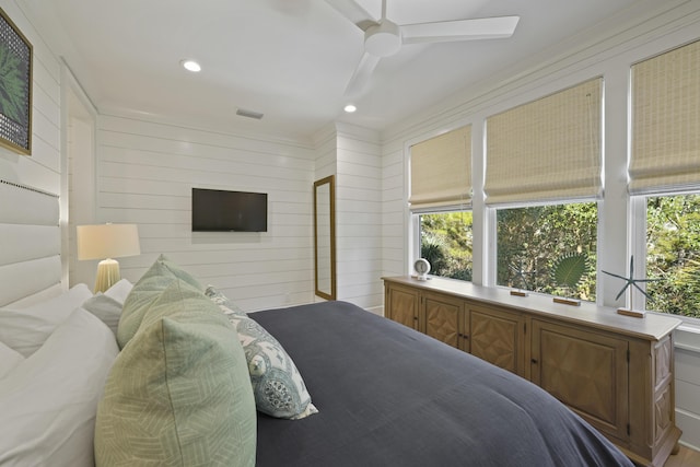 bedroom with ceiling fan, wooden walls, and crown molding