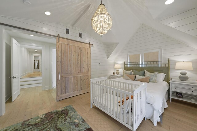 bedroom featuring an inviting chandelier, a barn door, light hardwood / wood-style flooring, wood walls, and vaulted ceiling