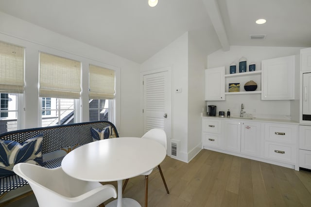 dining room featuring vaulted ceiling with beams, light wood-type flooring, and sink