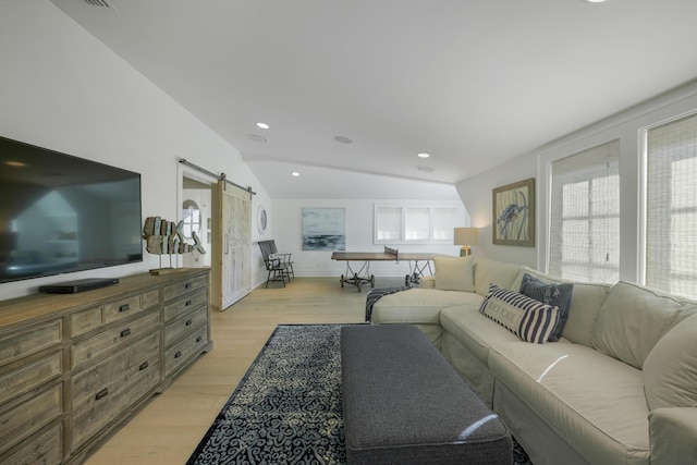 living room featuring light hardwood / wood-style floors, a barn door, a healthy amount of sunlight, and vaulted ceiling