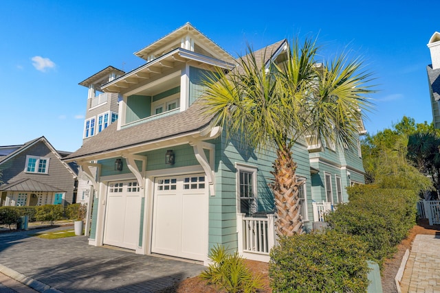 view of front of home with an attached garage, a shingled roof, and decorative driveway