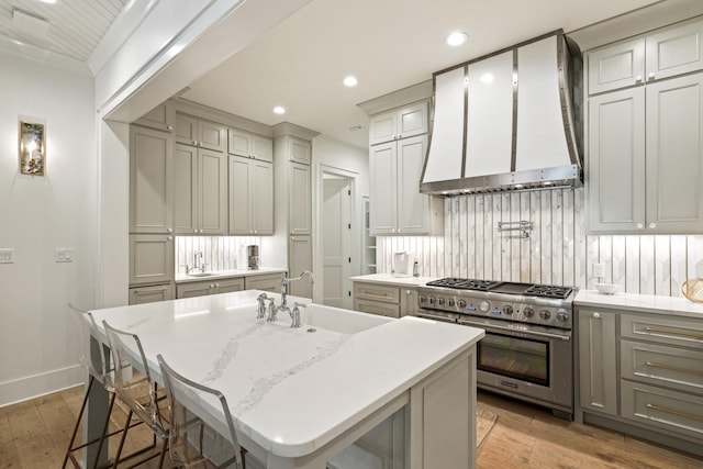 kitchen with wall chimney exhaust hood, high end stainless steel range, a sink, light wood-type flooring, and decorative backsplash