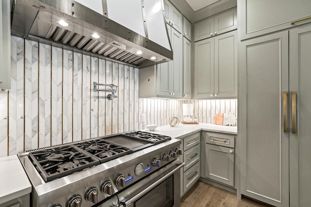 kitchen featuring wall chimney range hood, light wood-style floors, stainless steel range, light countertops, and gray cabinetry