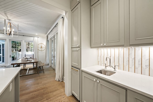 kitchen with a sink, light wood-style floors, a chandelier, pendant lighting, and gray cabinets
