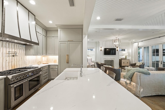 kitchen with wall chimney exhaust hood, a sink, open floor plan, visible vents, and premium appliances