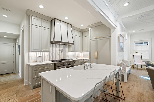 kitchen with premium appliances, backsplash, light wood-style floors, wall chimney exhaust hood, and gray cabinetry