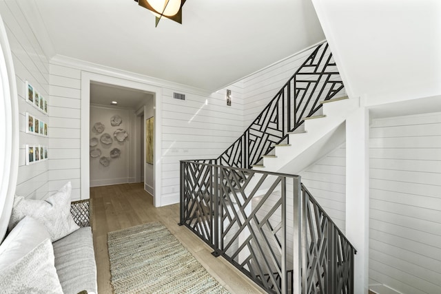 stairs featuring wood walls, ornamental molding, wood finished floors, and visible vents