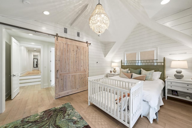 bedroom featuring lofted ceiling with beams, wood walls, a barn door, and hardwood / wood-style floors