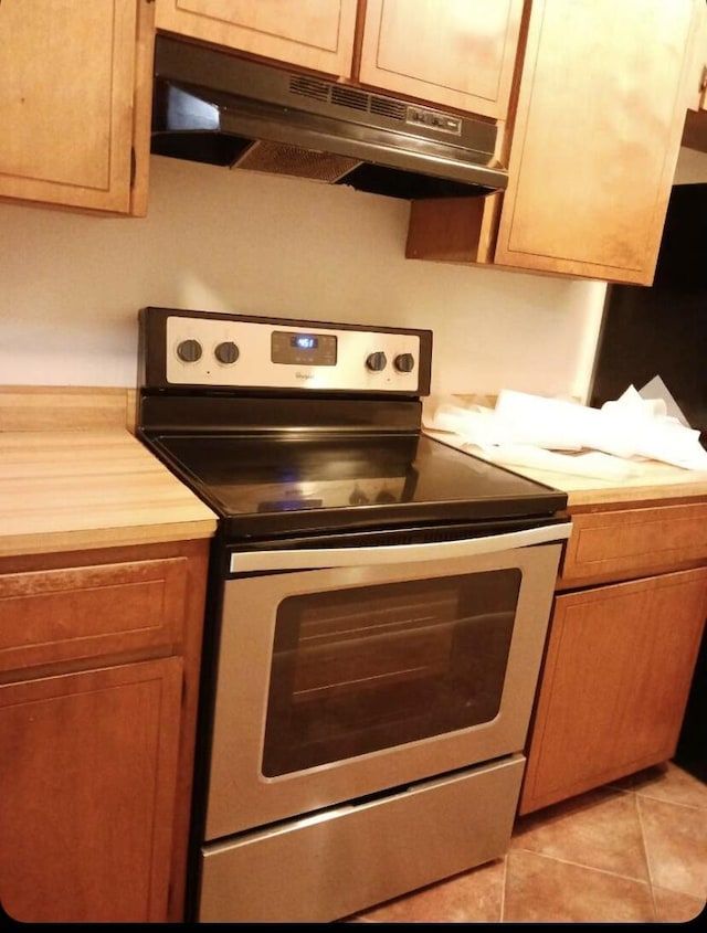 kitchen with stainless steel electric stove, light tile patterned floors, and wooden counters