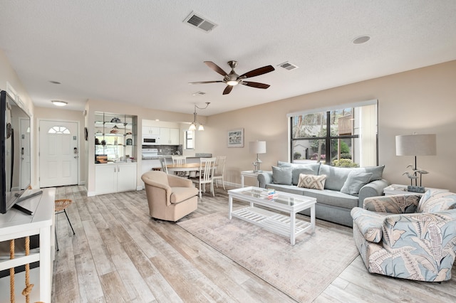 living room with a textured ceiling, light wood-type flooring, and ceiling fan